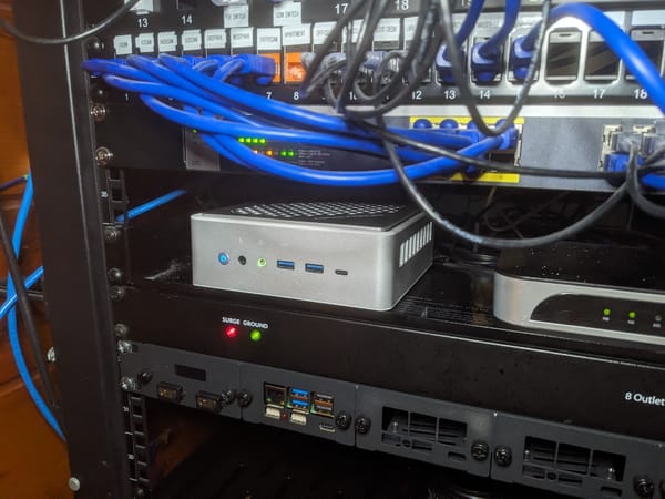 An Intel-based Minisforum mini PC running OPNSense sitting on a shelf in a server rack, surrounded by other network equipment.